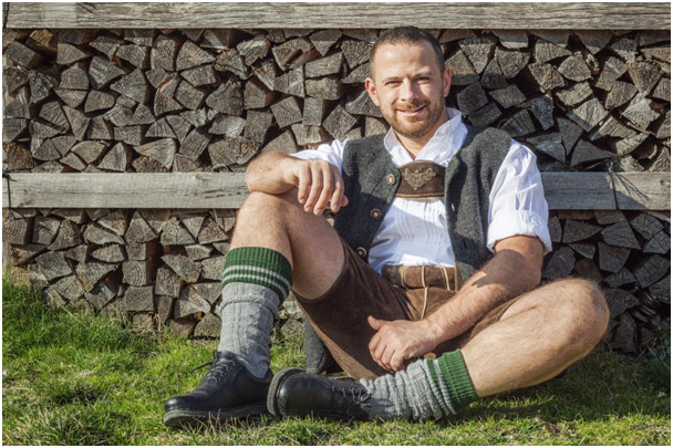 Mann in Lederhose bayrische Tracht, sitzend vor einem Holzstapel